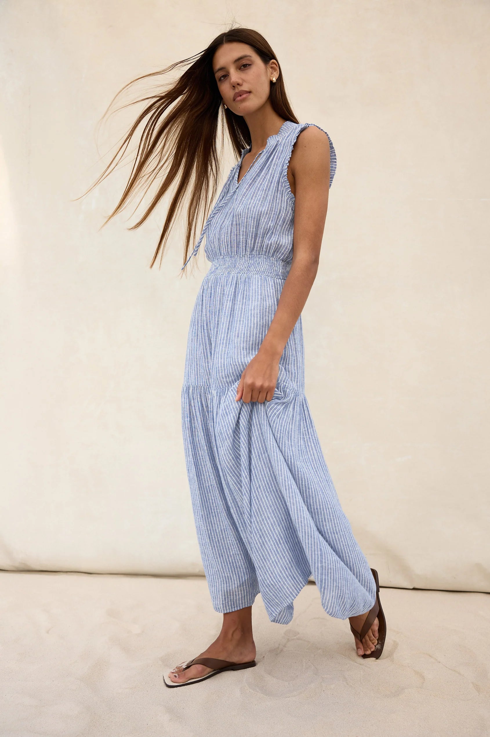 The Alessi is a luxe, lightweight linen midi dress with a relaxed fit, a split V-neckline with self-ties, a smocked waist, ruffle trim, and full lining.