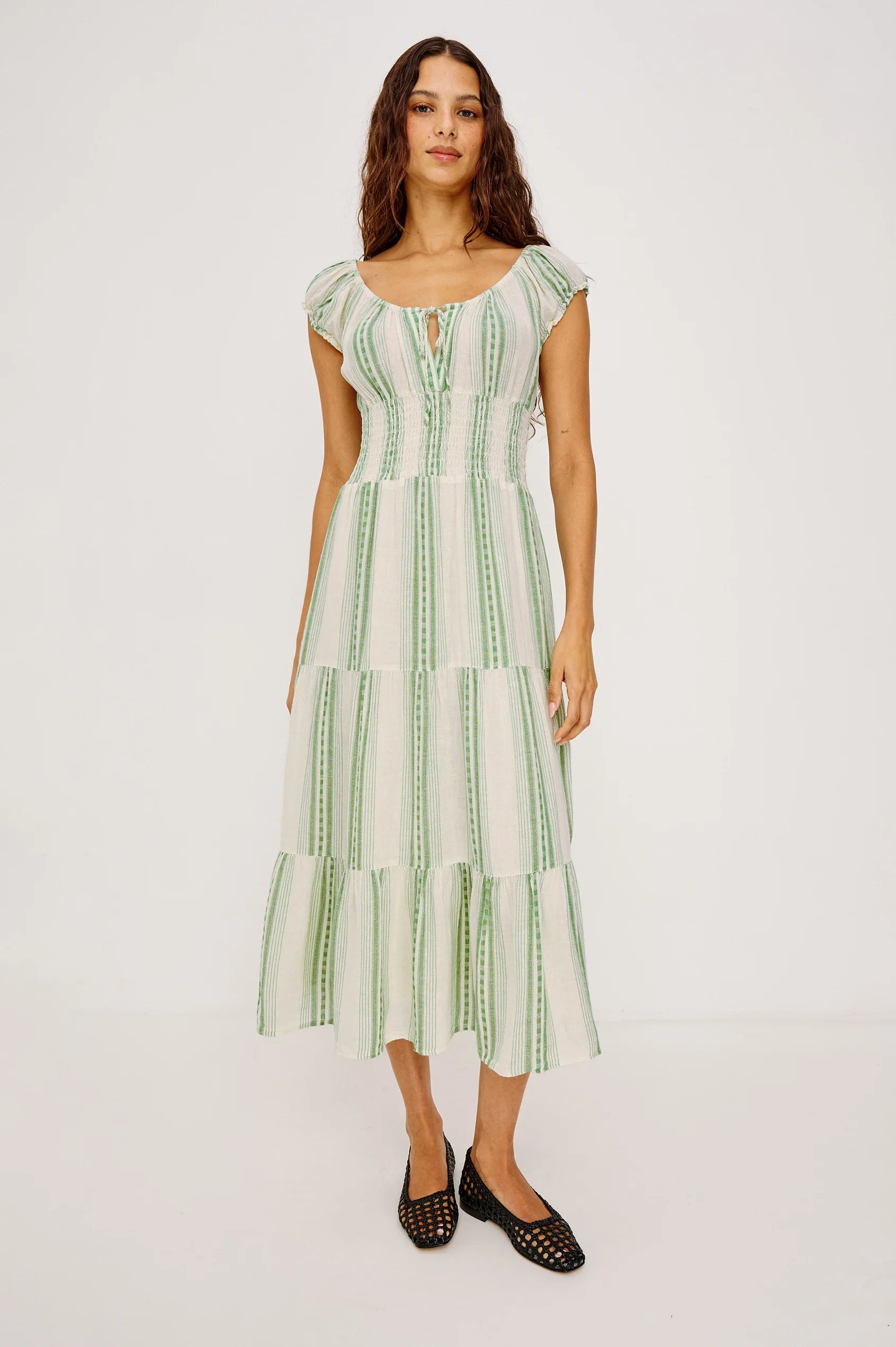 The Alessi is a luxe, lightweight linen midi dress with a relaxed fit, a split V-neckline with self-ties, a smocked waist, ruffle trim, and full lining.