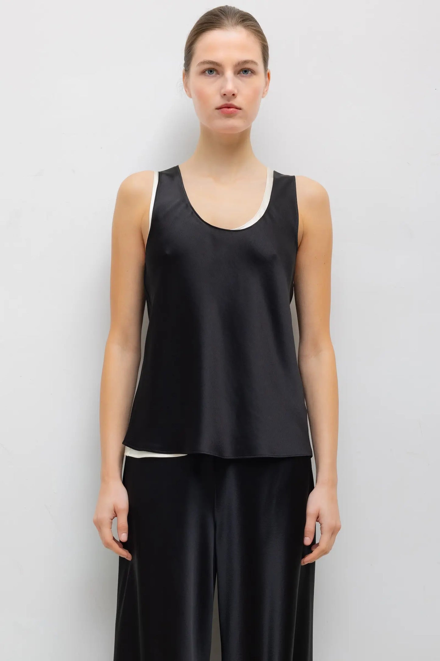 LESET Barb Bias Tank in black Japanese satin with scoop neckline, layered over ivory and styled with matching black satin pants.