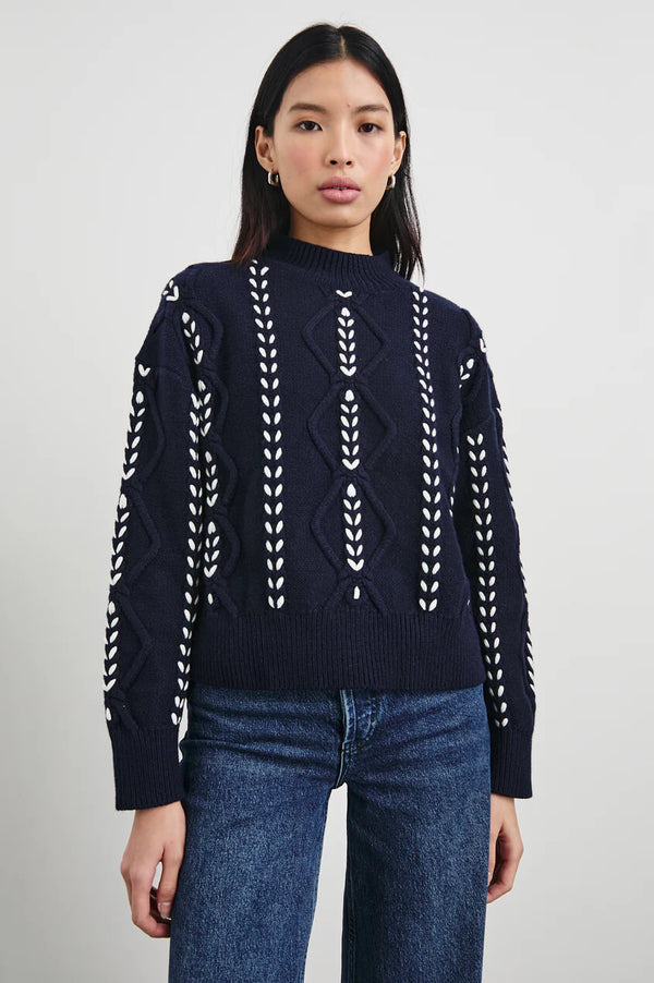 The Tori is an elevated take on the cable sweater, crafted from a heavy wool blend with a white contrast ribbon stitch, ribbed mock neck, and boxy fit.