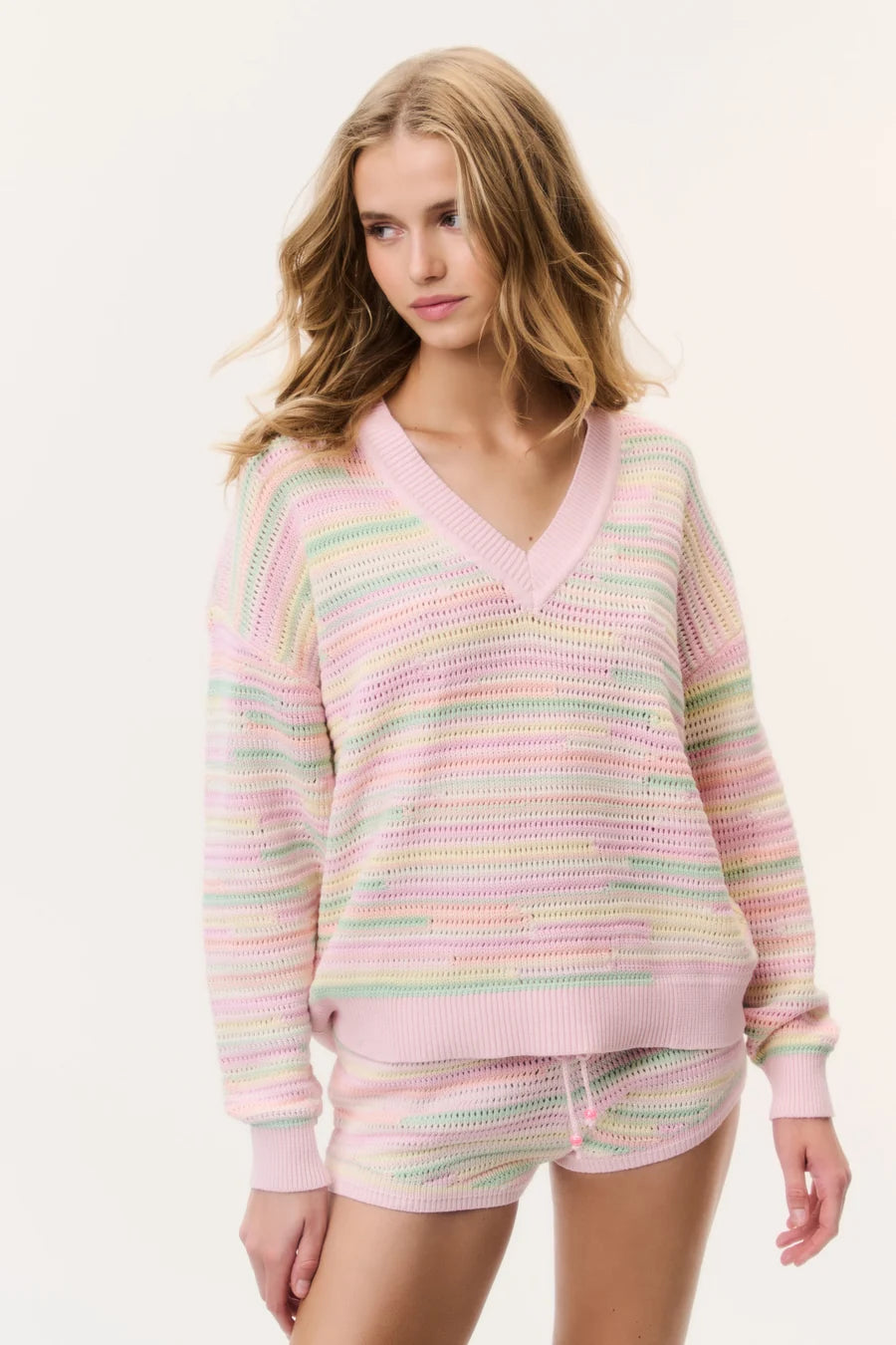 LoveShackFancy striped knit shorts in pastel pink, green and yellow with an elastic drawstring waist, styled with a matching V-neck sweater.