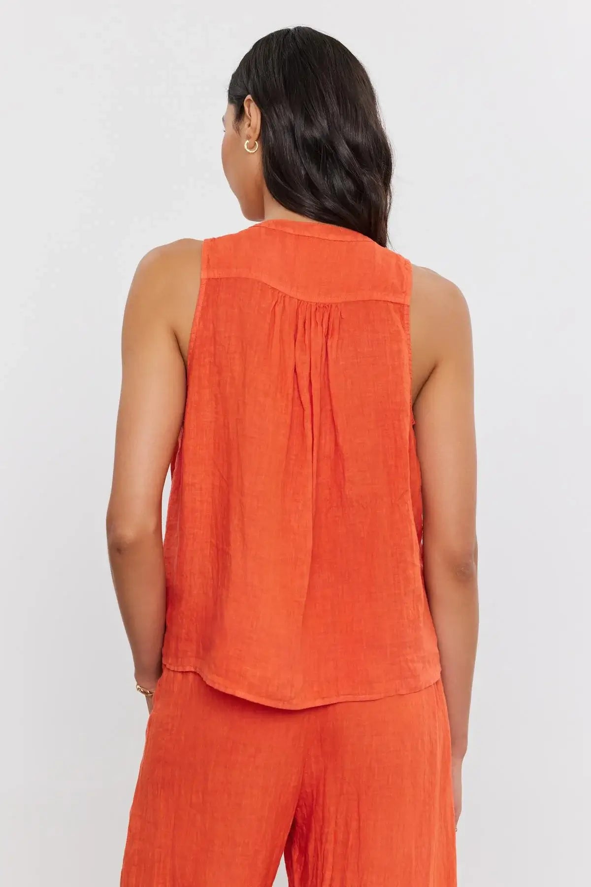 This woven linen sleeveless top features a flattering v-neckline and a relaxed fit, ideal for warm days and relaxed evenings. Complete with a high-low scooped hemline and shirred details on the rear, it's a versatile piece that effortlessly pairs with your favorite shorts or jeans for an easy-going look